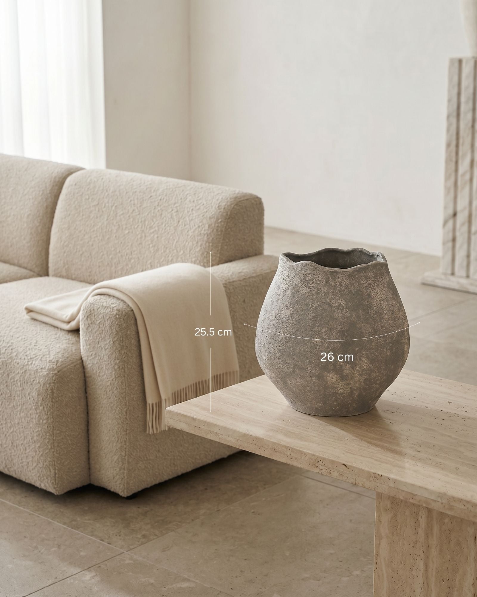 Beige sofa with a blanket and a stone vase on a wooden table in a minimalistic room.