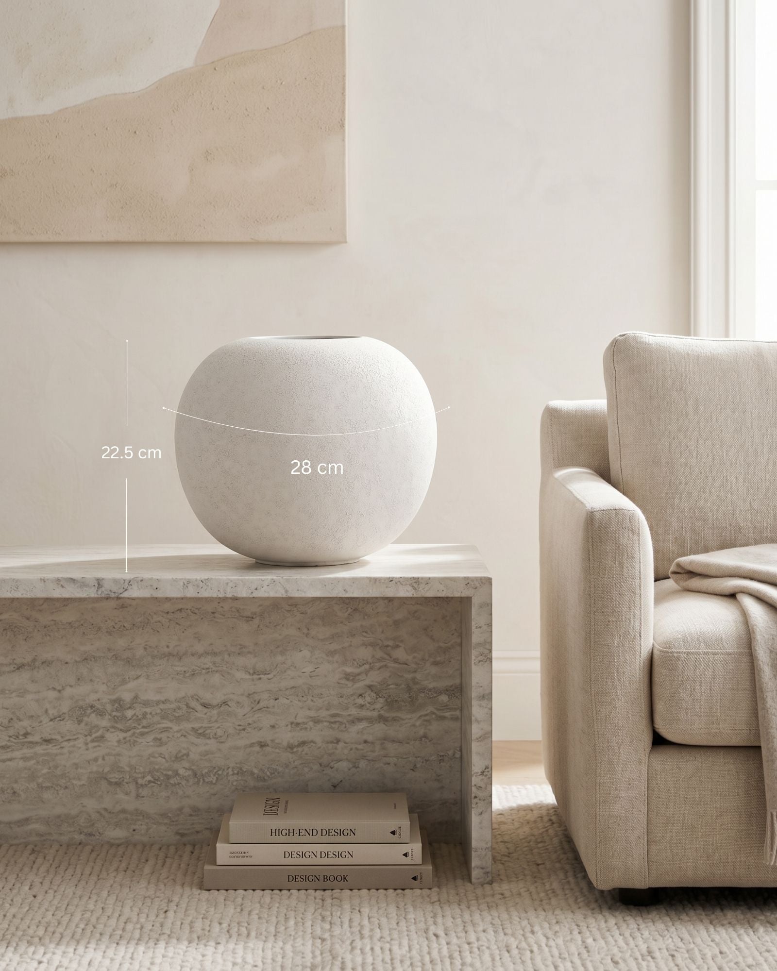 White spherical vase on a marble side table with a neutral-colored sofa and wall art in the background.
